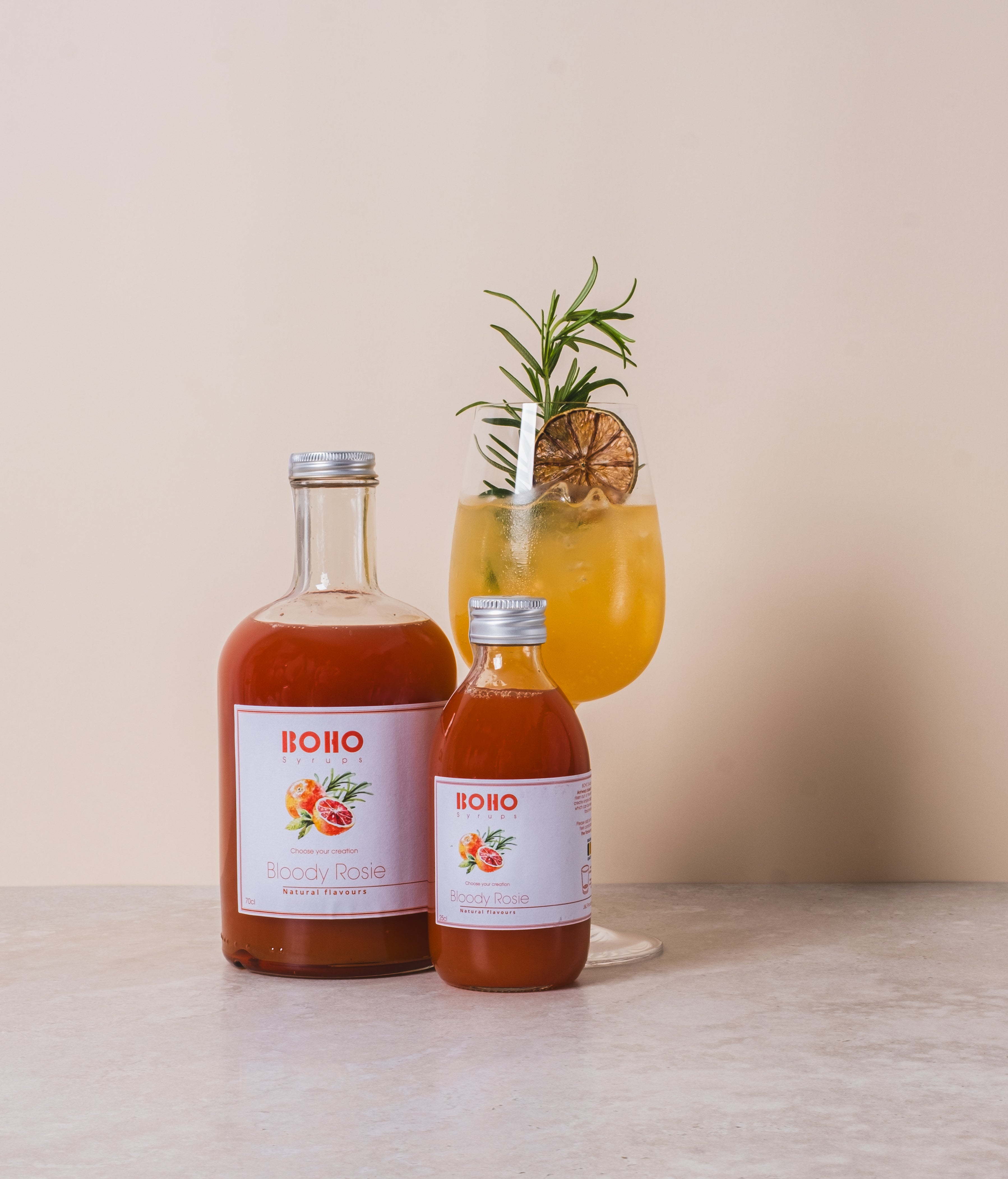 Fles BOHO bloedappelsien rozemarijn siroop met daarnaast een mooi gegarneerde mocktail – frisse en kruidige creatie