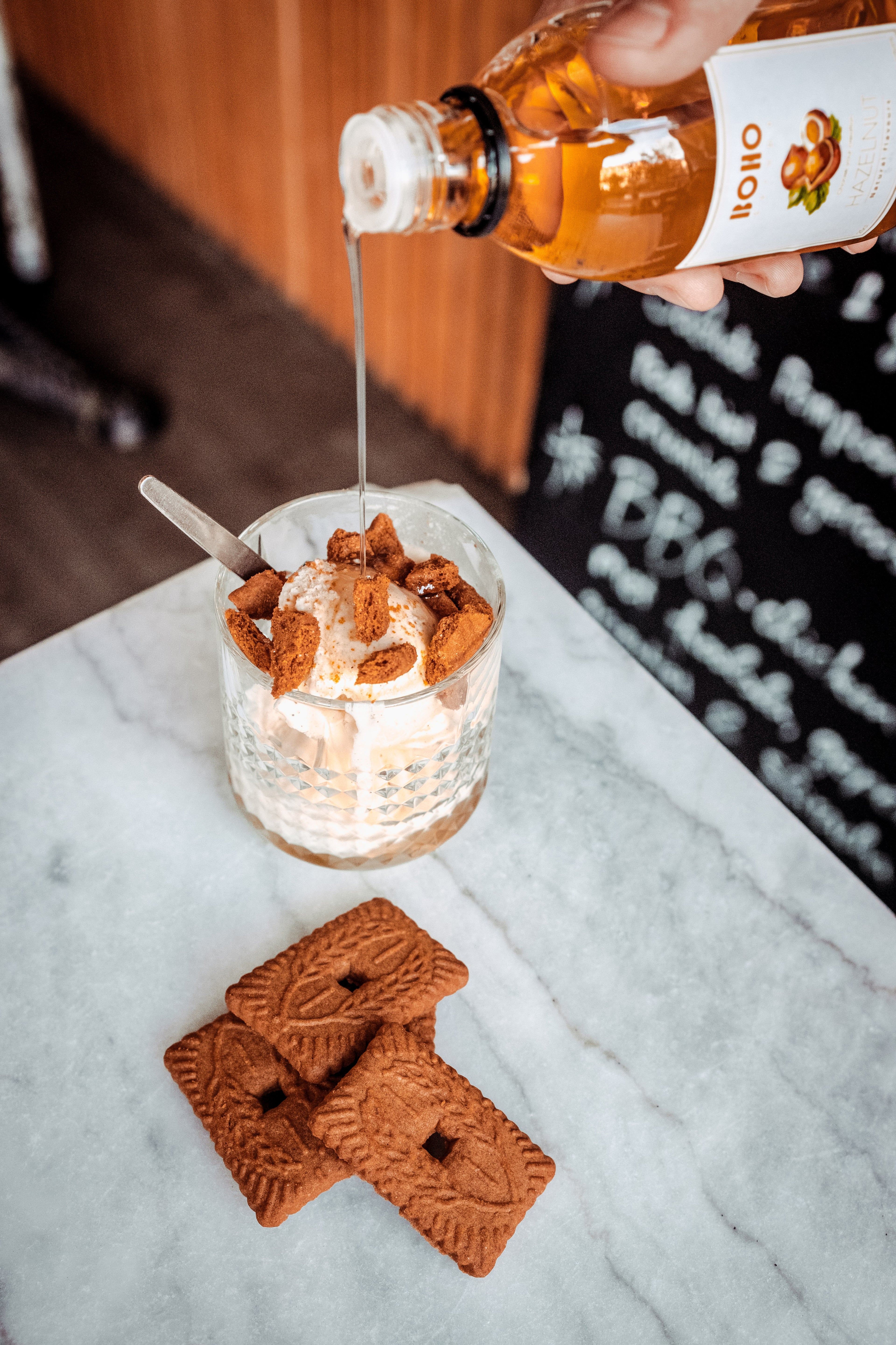 IJsje met stukjes speculaas waarover BOHO hazelnoot siroop wordt gegoten – romige en krokante dessertcombinatie