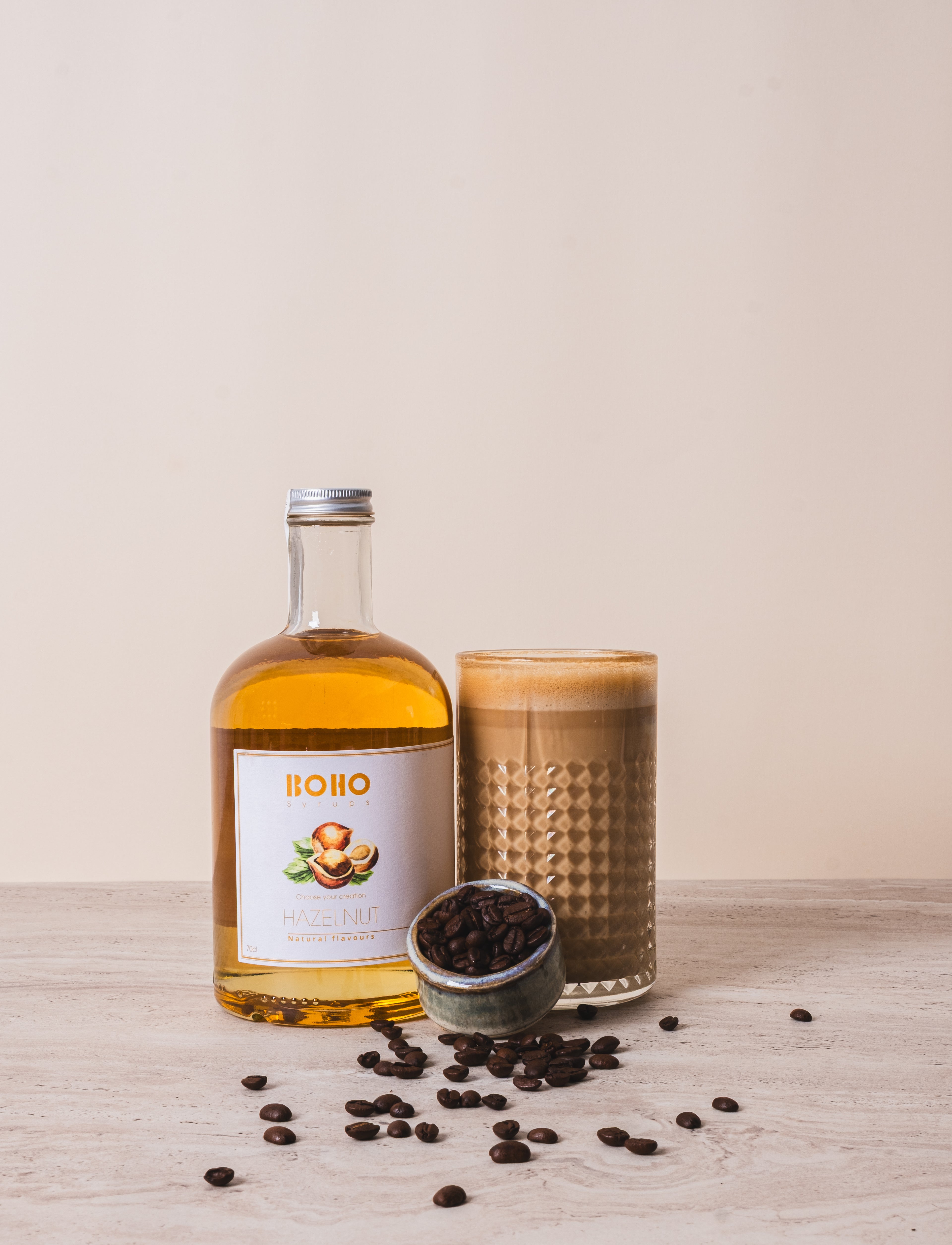 Grote fles BOHO hazelnoot siroop naast een latte macchiato – romige koffie met nootachtige toets