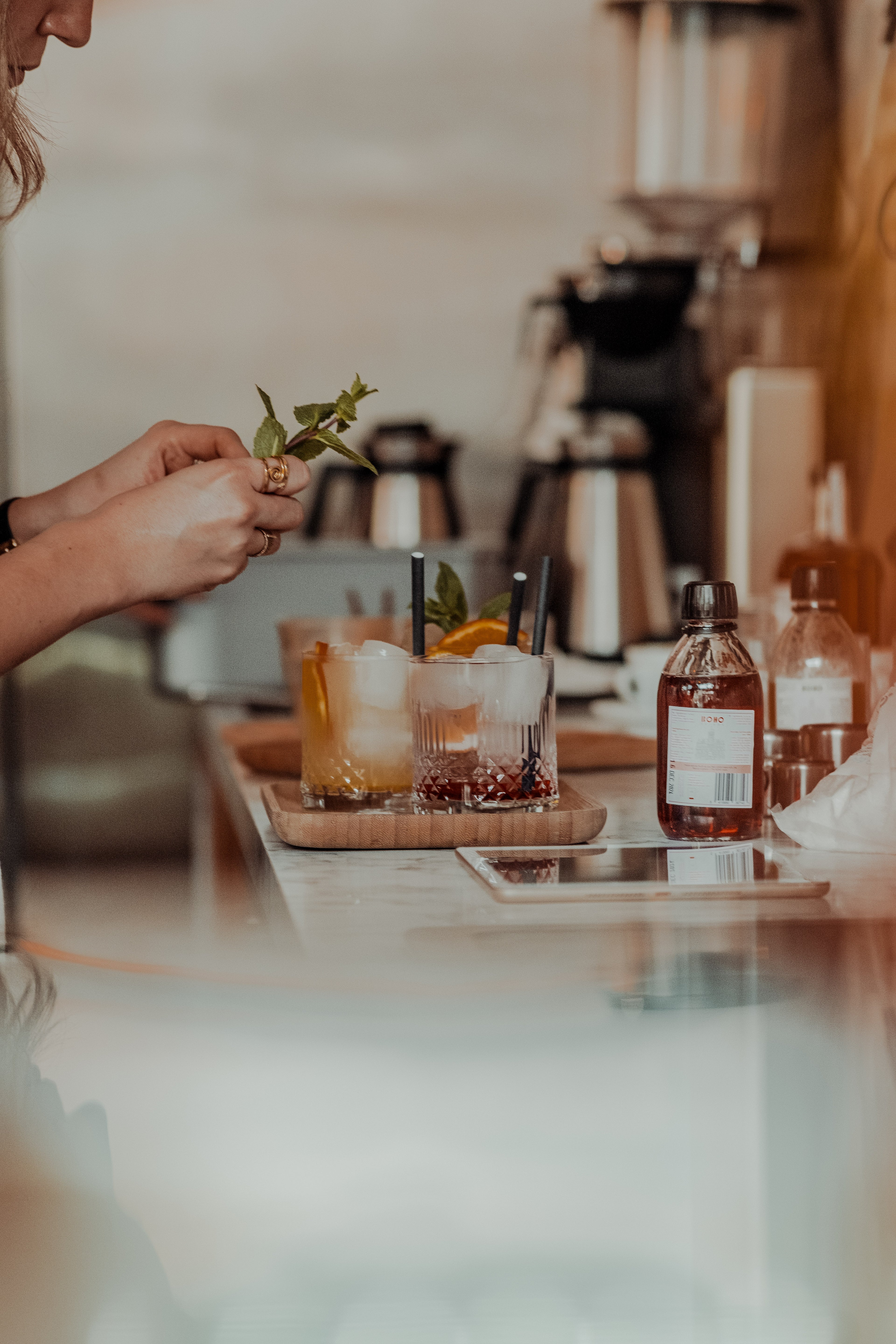 Barvrouw garneert twee homemade iced tea’s met een takje munt, gemaakt met BOHO Syrups – verfrissend en ambachtelijk