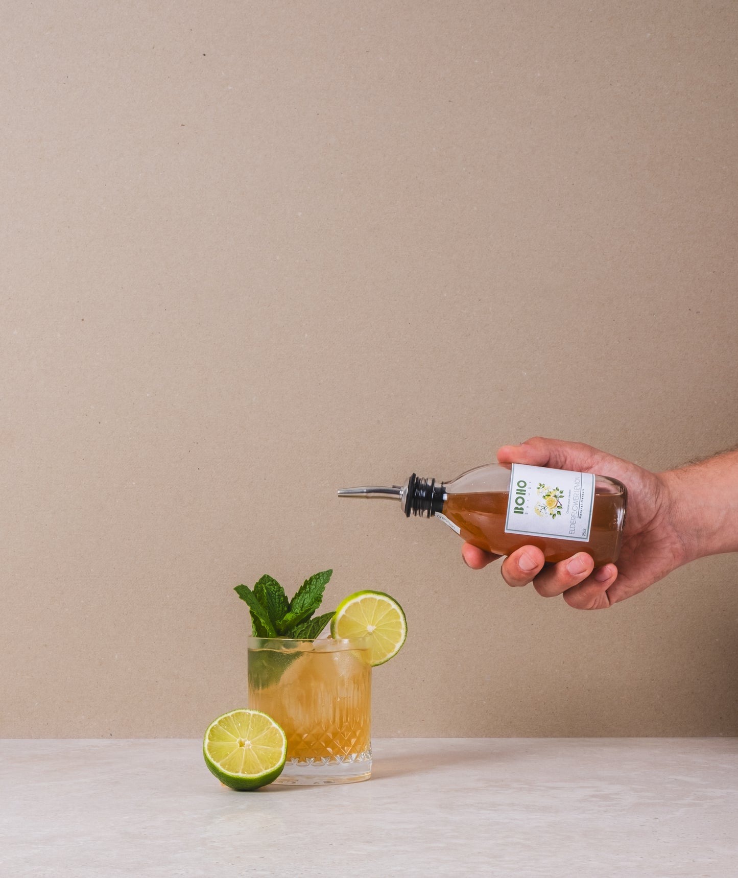 Glas homemade limonade waarin BOHO vlierbloesem citroen siroop uit een flesje wordt ingeschonken – frisse en bloemige zomersmaak